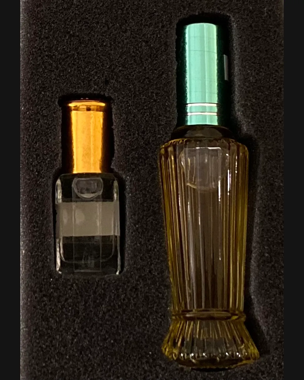 A ribbed glass bottle and a small vial seated side by side in a black foam tray