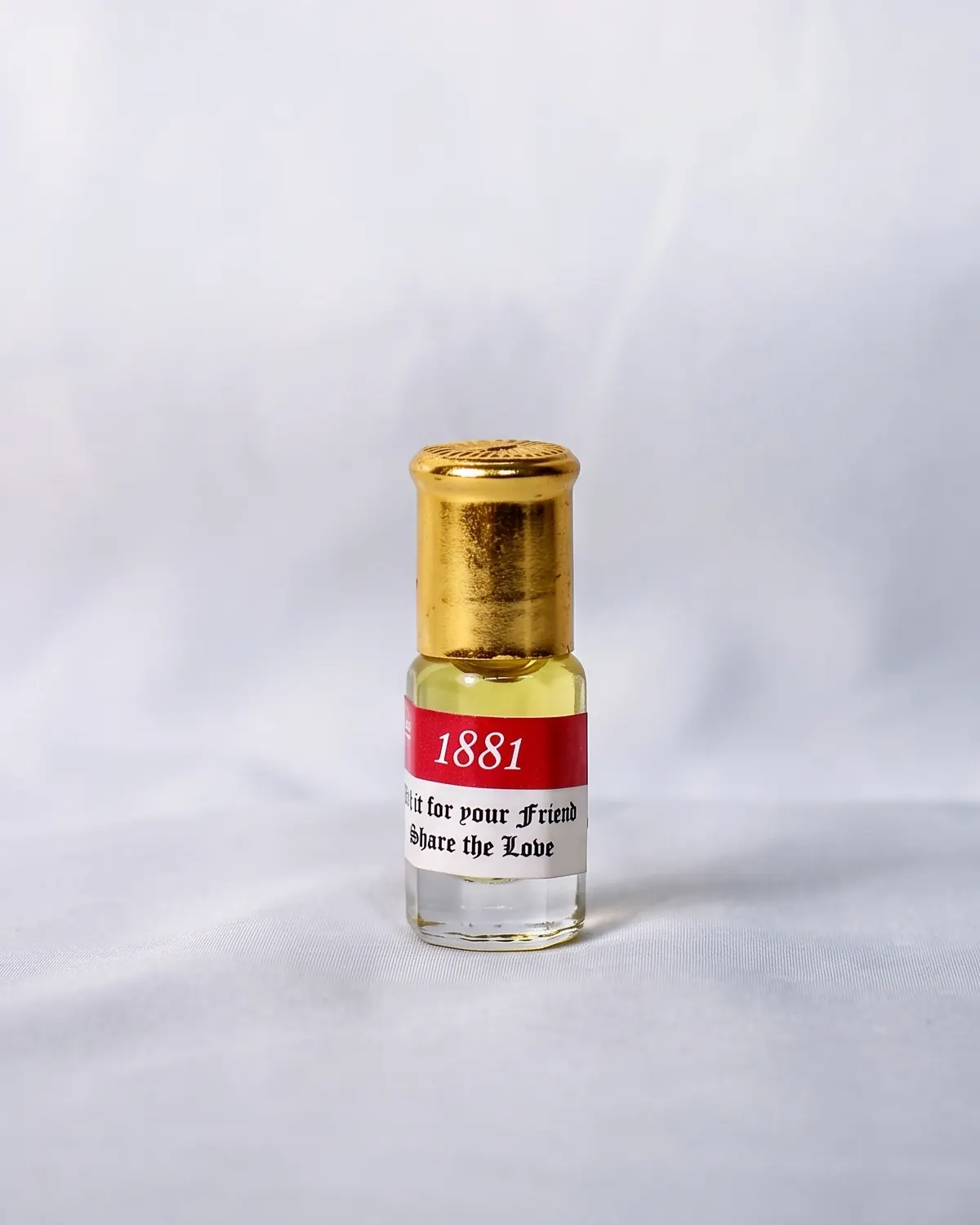 A small glass vial of perfume oil with a gold cap, standing on white cloth