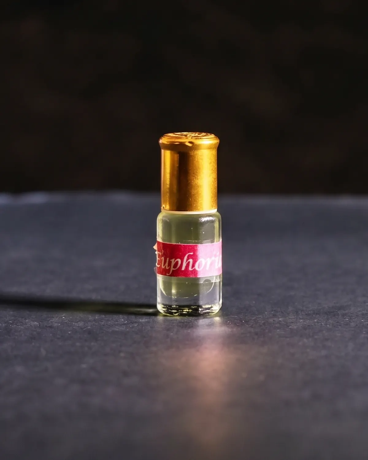 A small glass vial of perfume oil with a gold cap on a dark slate surface